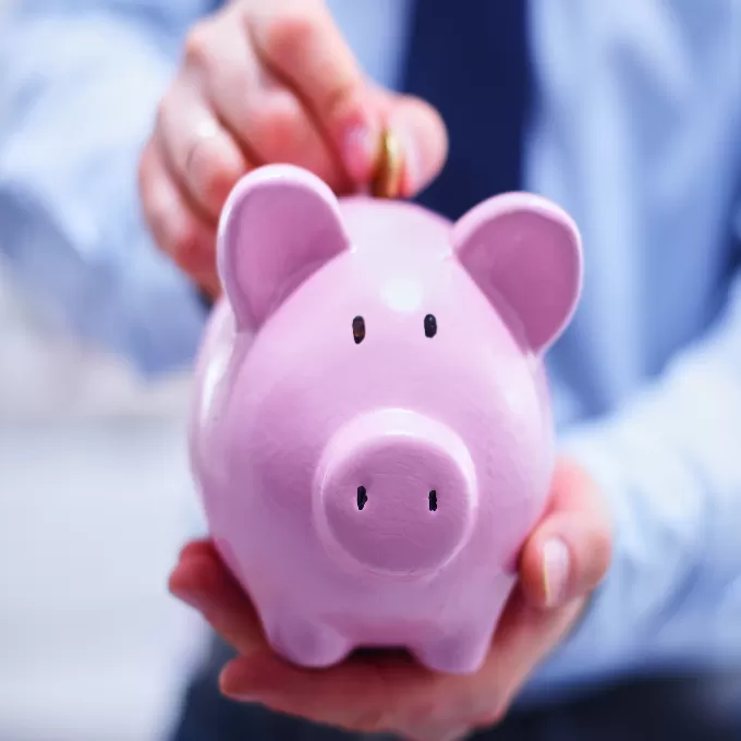 A man inserting a pound coin into a piggy bank.
