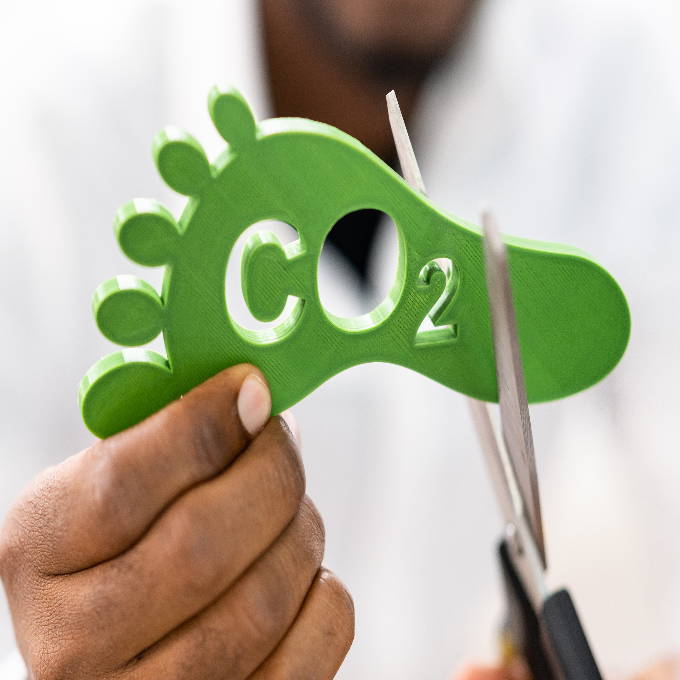 A man using a pair of scissors to cut into a foot made of polyester with 'CO2' written on it, symbolising carbon cutting.